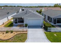 Charming single-story home with a well-manicured lawn, white picket fence, and attached two-car garage at 8233 Se 169Th Palownia Loop, The Villages, FL 32162