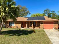 Charming brick home featuring solar panels, a well-manicured lawn, and a lovely palm tree at 1062 Stillwater Ave, Deltona, FL 32725