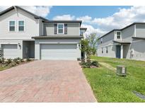 Charming townhome featuring a brick driveway, two-car garage, and neutral-toned siding under a bright, partly cloudy sky at 16450 Bird Of Paradise Ave, Clermont, FL 34714