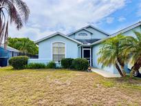 Charming single story blue home with manicured lawn, complimented by palm trees under a cloudy blue sky at 72 Saint Kitts Cir, Winter Haven, FL 33884