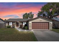 Charming single-story home with a well-manicured lawn, two-car garage, and a brick facade against a sunset sky at 2955 Foxcroft Ln, South Daytona, FL 32119