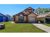 Charming tan two-story home with a well-manicured lawn and attached one car garage on a sunny day at 10020 Creekwater Blvd, Orlando, FL 32825