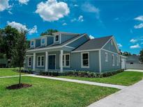Charming two-story home features dormer windows, blue siding, a well-manicured lawn, and a welcoming front porch at 311 W Delaware Ave, Lake Helen, FL 32744