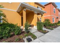 Inviting townhome entrance featuring a well-manicured landscape, covered porch, and cheerful, warm exterior color at 8963 Majesty Palm Rd, Kissimmee, FL 34747