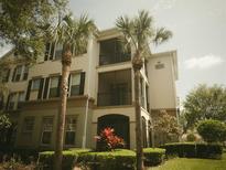 Three-story condo building with a beige facade, black shutters, well-manicured landscaping, and two palm trees at 8276 Maritime Flag St # 201, Windermere, FL 34786