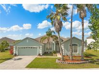 Charming home with a two-car garage, manicured lawn, and mature palm trees on a sunny day at 5335 Coral Vine Ln, Kissimmee, FL 34758