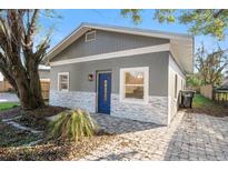 Charming gray home featuring a blue door, stone accents, and a well-maintained brick driveway at 1321 Cloverlawn Ave, Orlando, FL 32806