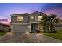 Charming two-story home with a tile roof, lush landscaping, and a paver driveway at dusk at 1158 Oak Bluff Dr, Davenport, FL 33837