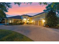 Elegant home with a three-car garage, paver driveway, manicured landscaping, and a tile roof set against a beautiful sunset sky at 11954 Provincial Way, Windermere, FL 34786