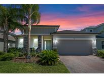 Charming single-story home with a two-car garage, landscaped yard, and brick-paved driveway during a vibrant sunset at 861 Grazie Loop, Davenport, FL 33837