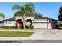 Charming single-story home with a well-manicured lawn and a two-car garage. Has a bright red front door and palm tree at 10827 Lemay Dr, Clermont, FL 34711