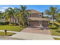 Charming two-story home featuring mature palm trees, a well-manicured lawn, and a three car garage on a brick driveway at 920 Nola Dr, Ocoee, FL 34761