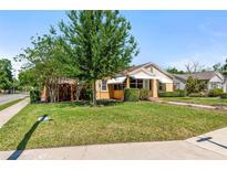 Beautifully landscaped front yard with mature trees and green lawn, with yellow home exterior and awnings at 335 W Bay St, Winter Garden, FL 34787