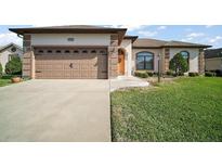 Inviting single-story home featuring a well-manicured lawn, a two-car garage and an arched entry with a wreath at 11041 Se 169Th Pl, Summerfield, FL 34491