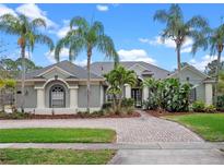 Charming single-story home featuring lush tropical landscaping, a brick driveway, and a stylish gray and white color scheme at 2218 Ridgewind Way, Windermere, FL 34786