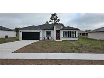 Charming single-story home featuring a dark garage door, orange front door, and freshly installed landscaping at 699 Marion Oaks Trl, Ocala, FL 34473