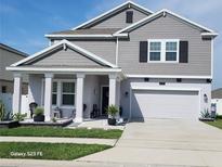 Charming two-story home featuring gray siding, a covered porch with white columns, and an attached two-car garage at 1803 Perch Hammock Loop, Groveland, FL 34736