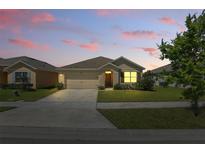 Charming one-story home with a well-manicured lawn, two car garage, and inviting front entrance at dusk at 3348 Perennial Ln, Kissimmee, FL 34746