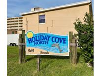 Holiday Cove North rental sign with dolphin against a tan building with nice grass at 573 N Atlantic Ave # 5, New Smyrna Beach, FL 32169