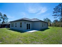 An expansive backyard features a concrete patio with sliding glass doors and a meticulously maintained lawn, perfect for outdoor living at 5 Fisher Loop, Ocklawaha, FL 32179