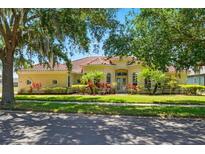 Charming yellow house with a red tile roof, complemented by lush landscaping and mature trees at 12614 Hawkstone Dr, Windermere, FL 34786