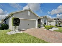 Charming single-story home featuring a brick driveway, manicured lawn, gray facade, and two-car garage at 299 Whirlaway Dr, Davenport, FL 33837