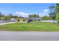 Charming yellow single-story home with a large grassy front yard, palm tree, and an American flag at 5800 Spruce Creek Woods Dr, Port Orange, FL 32127