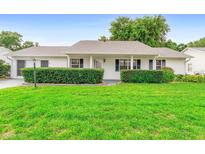 Charming single-story home with a well-manicured lawn, neat shrubbery, and a covered front porch at 25929 Newcombe Cir, Leesburg, FL 34748