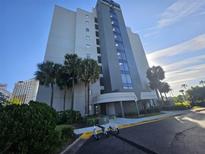 Modern condo building featuring a sleek design, palm trees, scooters parked out front, and a bright sunny sky at 6165 Carrier Dr # 3201, Orlando, FL 32819