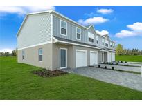 View of townhomes with one car garages, blue siding, paved driveways, and green lawns on a sunny day at 1419 Fan Palm Dr, Davenport, FL 33897