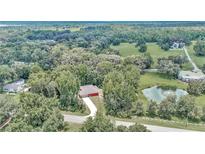 A scenic aerial view of a red home nestled amongst lush green trees with a pond nearby at 6144 Avenue G, Mc Intosh, FL 32664