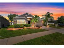 Charming single-story home featuring a well-manicured lawn, tropical landscaping, and brick accents at sunset at 4027 Sunrise Ridge Blvd, Groveland, FL 34736
