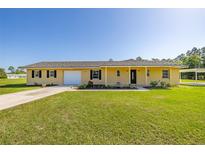 Charming single-story home featuring a well-manicured lawn, attached garage, and covered parking space at 6273 Toronja Dr, Indian Lake Estates, FL 33855