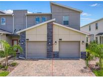 A modern townhome boasts a two-car garage with brick driveway and stone accents, complemented by lush palm trees at 507 Ocean Course Ave # 507, Davenport, FL 33896