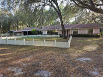 Charming single-story home featuring mature trees, a white picket fence, and a covered parking area at 9741 Se Highway 464C Se Hwy, Ocklawaha, FL 32179