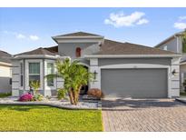 Charming gray home featuring manicured lawn, beautiful landscaping, brick driveway, and two-car garage at 1210 Pando Loop, Orlando, FL 32824