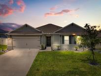 Charming single-story home featuring a well-manicured lawn, inviting entrance, and a two-car garage at twilight at 445 Auburn Grove Pl, Auburndale, FL 33823