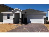 Charming one-story home with brick-paved driveway, gray roof, and stone-accented columns at 7138 Rolling Leaf Rd, Groveland, FL 34736