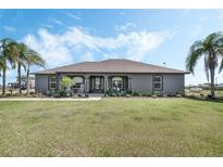 Charming gray home featuring a well-manicured lawn, inviting front porch with rocking chairs, and mature palm trees at 4400 Walker Lake Rd, Bartow, FL 33830