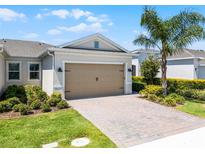Home featuring a spacious garage, a paver driveway, and beautiful landscaping with a mature palm tree in the front yard at 2026 Key Bay Trl, Kissimmee, FL 34747
