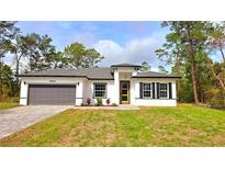 Charming single-story home with a gray driveway, inviting yellow front door, and well-maintained landscaping at 16908 Sw 44Th Cir, Ocala, FL 34473