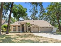 Charming single-story home with three-car garage, mature trees, and a well-manicured lawn under a clear blue sky at 2082 Nexus Ct, Apopka, FL 32712