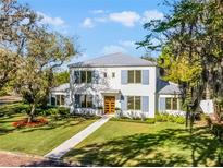 Elegant two-story home featuring a manicured lawn, blue shutters, and a light gray metal roof at 2171 Forrest Rd, Winter Park, FL 32789