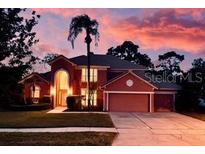 Charming two-story home with a well-manicured lawn, mature trees and a colorful, vibrant sunset in the background at 3020 Zaharias Dr, Orlando, FL 32837