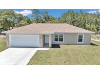 Inviting single-story home featuring a neatly manicured lawn, attached garage, and light beige exterior at 3914 Sw 161St Loop, Ocala, FL 34473