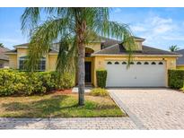 Charming yellow single-story home with a two-car garage, lush landscaping, and a brick paver driveway at 650 Old Bridge Cir, Davenport, FL 33897