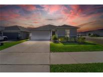 Charming single-story home featuring a two-car garage, well-manicured lawn, and inviting curb appeal under a vibrant sunset sky at 820 Overpool Ave, Davenport, FL 33896