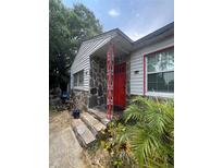 Charming home featuring a stone facade, red door, and decorative support beams at 7506 Mott Ave, Orlando, FL 32810