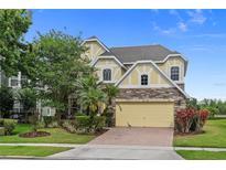 Charming two-story home features a stone facade, yellow accents, well-manicured landscaping, and a brick driveway at 850 Spring Oak Cir, Orlando, FL 32828