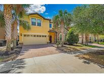 Two-story home with a two-car garage, brick driveway, stone accents, and lush landscaping with palm trees at 8804 Rhodes Street, Kissimmee, FL 34747